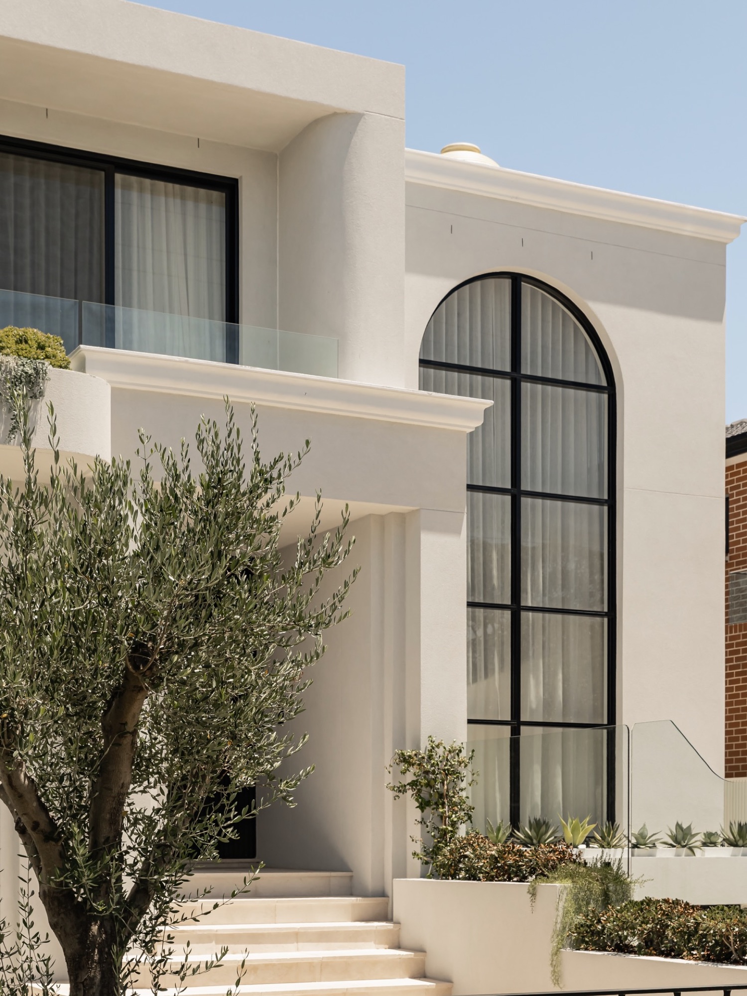 Facade detail — arched steel window, moulded cornice and olive tree