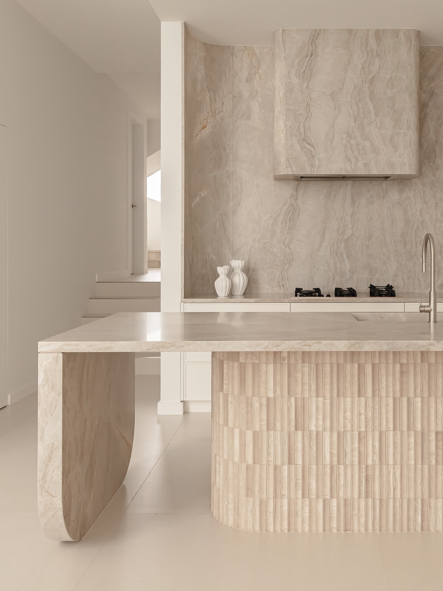 Kitchen with figured stone splashback, stone hood and fluted travertine island