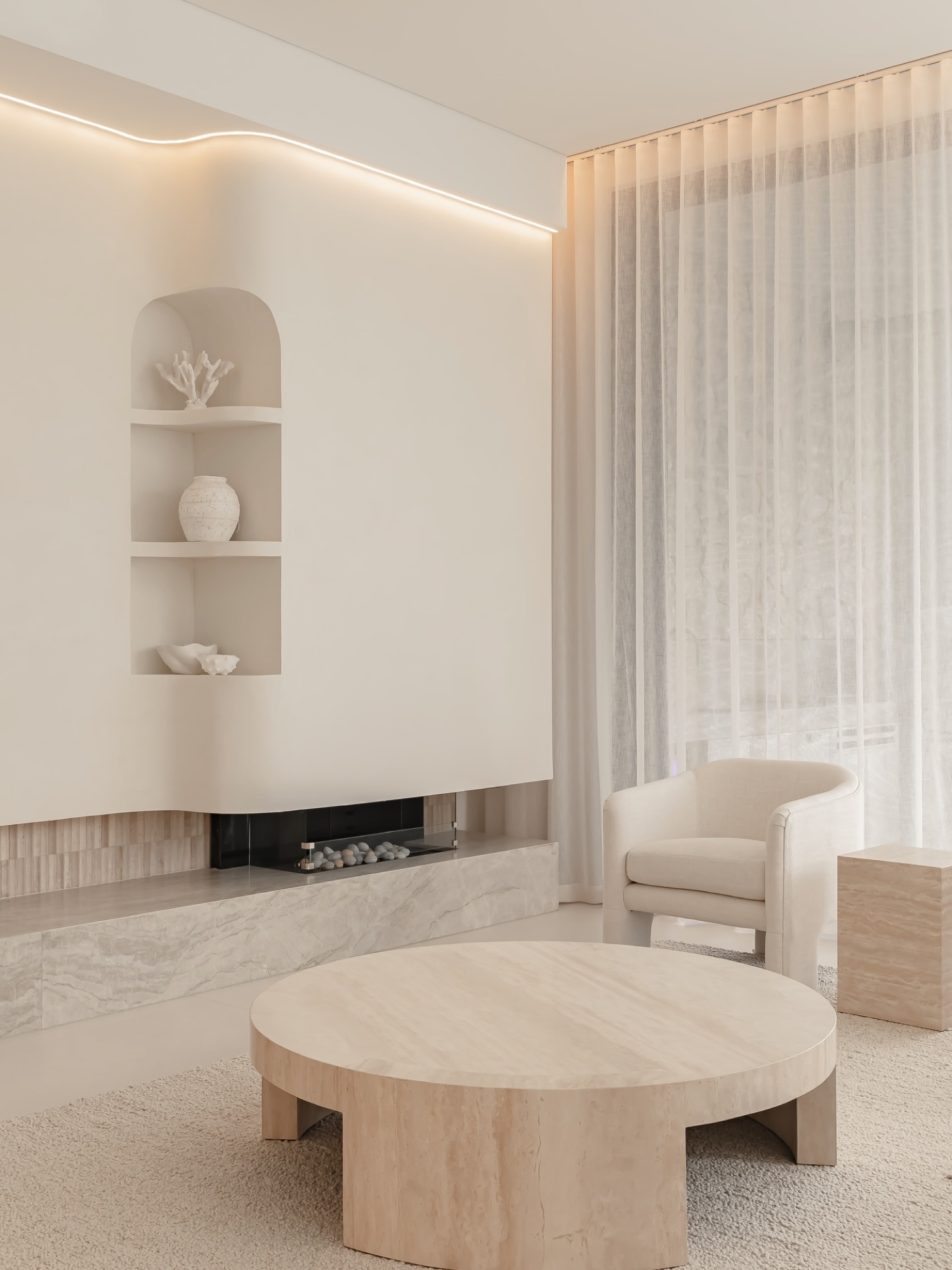 Living room with round travertine table, linear fireplace and arched display niche